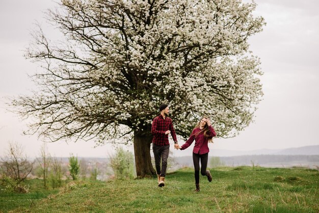 Giovani coppie romantiche che camminano sul prato e sull'albero in fiore e si divertono