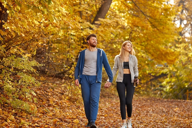 Giovani coppie romantiche che godono della passeggiata nella foresta soleggiata di autunno, contemplando la natura, alberi gialli intorno. escursionismo, bosco autunnale, passeggiate, concetto di amore