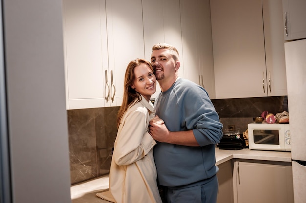 Giovani coppie sexy romantiche che passano felicemente il tempo abbracciandosi e baciandosi nell'accogliente cucina moderna a casa Due persone stanno in piedi e si guardano con gioia