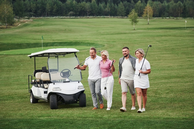 Giovani coppie si preparano a giocare. Un gruppo di amici sorridenti venne alla buca su un carrello da golf