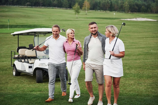 Giovani coppie si preparano a giocare. Un gruppo di amici sorridenti venne alla buca su un carrello da golf