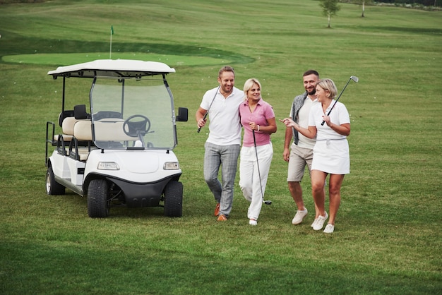 Giovani coppie si preparano a giocare. Un gruppo di amici sorridenti venne alla buca su un carrello da golf