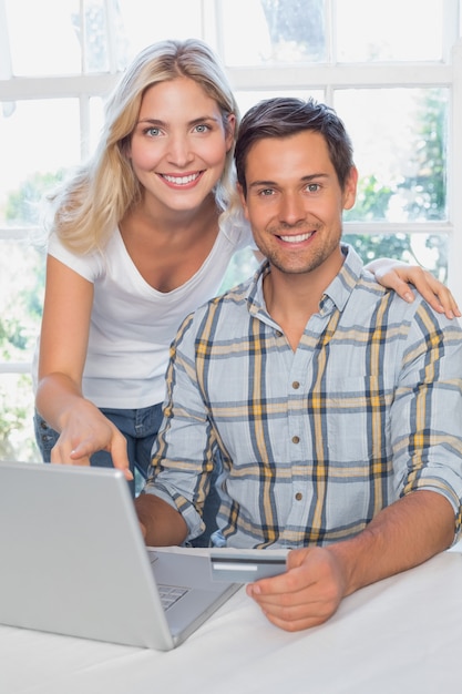 Giovani coppie sorridenti che fanno compera online a casa