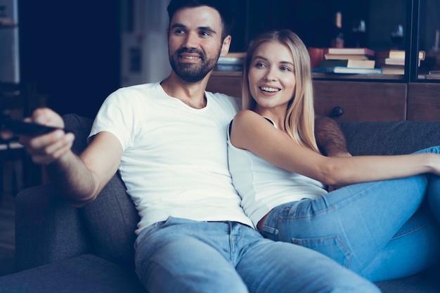 Giovani coppie sorridenti che si rilassano e che guardano la TV a casa.