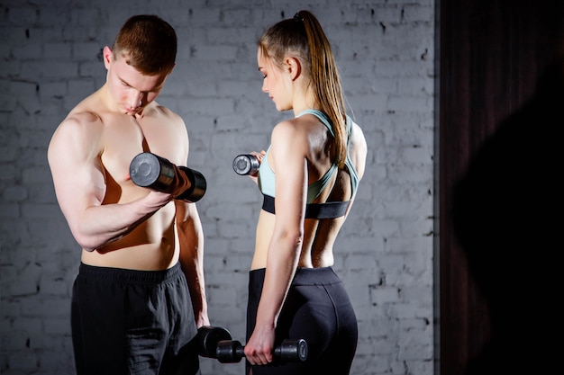 Giovani coppie sveglie che si esercitano con i dumbbells in ginnastica