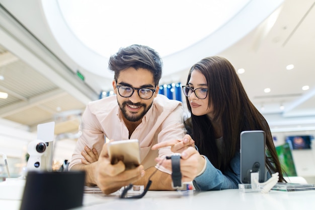 Giovani coppie sveglie in deposito elettronico che collauda alcuni nuovi telefoni. Alla ricerca dell'attrezzatura ideale.