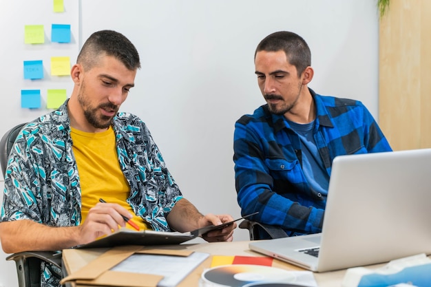 Giovani designer felici nell'ufficio di avvio che lavorano su laptop Uomini d'affari con adesivi post-it