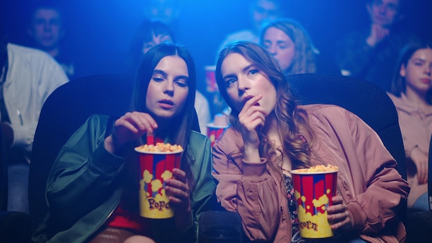 Giovani donne che mangiano uno spuntino al cinema Fidanzate carine che si rilassano con i popcorn