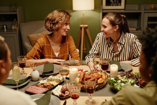 Giovani donne che parlano tra loro mentre si siedono al tavolo da pranzo con i loro amici durante la cena a casa