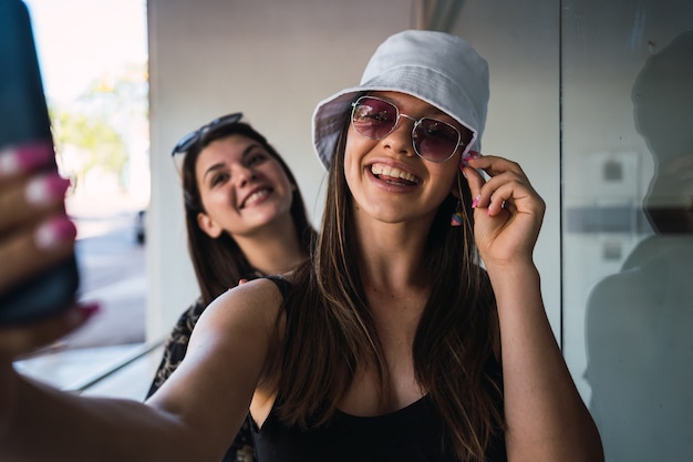 Giovani donne che prendono un selfie all'aperto - Due adorabili amici con occhiali da sole che sorridono per il selfie.