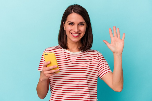 Giovani donne che tengono telefono cellulare sorridente allegro che mostra numero cinque con le dita.