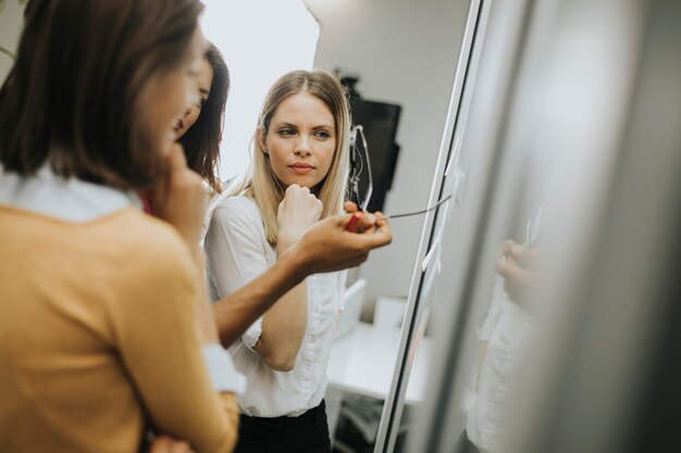 Giovani donne d'affari discutendo davanti alla parete di vetro usando post-it note e adesivi