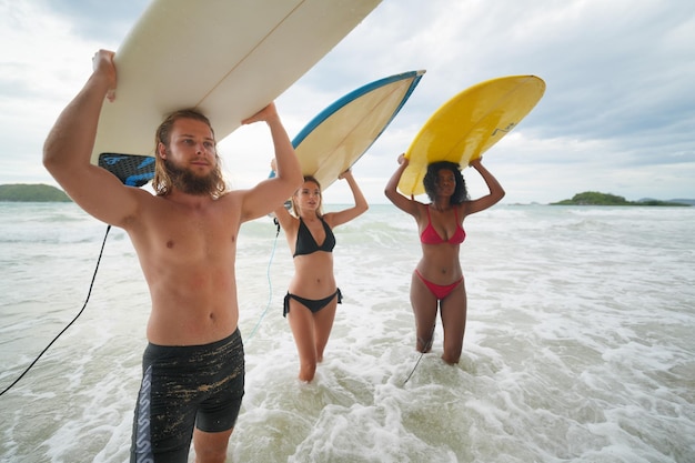 Giovani donne di razza mista e donne e uomini caucasici che si divertono in spiaggia con i loro amici che tengono tavole da surf