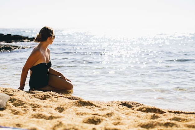 Giovani donne in costume da bagno che si siede nella sabbia in riva al mare