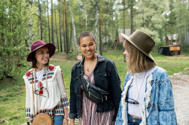 Giovani donne interrazziali positive in abiti hippie che camminano insieme mentre si godono le vacanze al campeggio