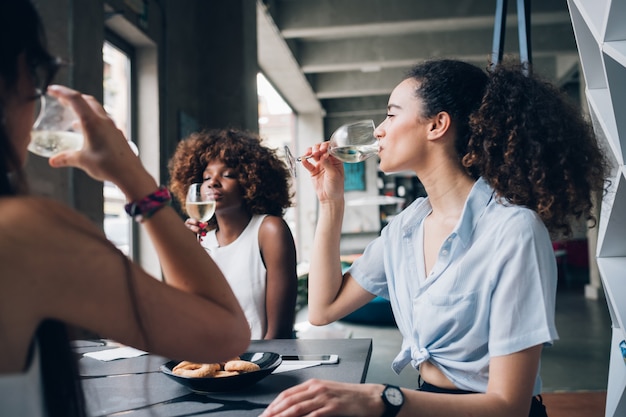 Giovani donne multirazziali che si siedono nel ristorante moderno che bevono insieme vino