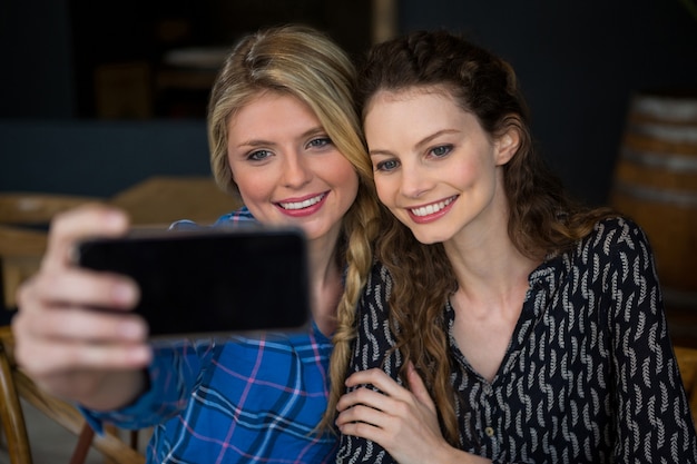 Giovani donne sorridenti che prendono selfie tramite smart phone nella caffetteria
