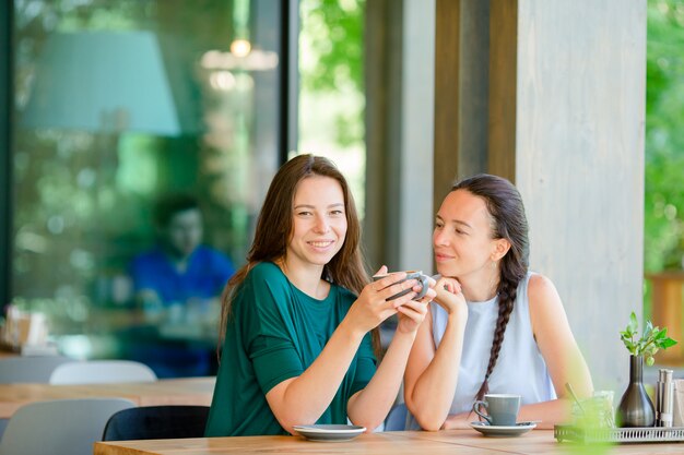 Giovani donne sorridenti felici con le tazze di caffè al caffè. Concetto di comunicazione e amicizia