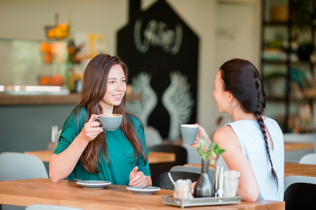 Giovani donne sorridenti felici con le tazze di caffè al caffè. Concetto di comunicazione e amicizia