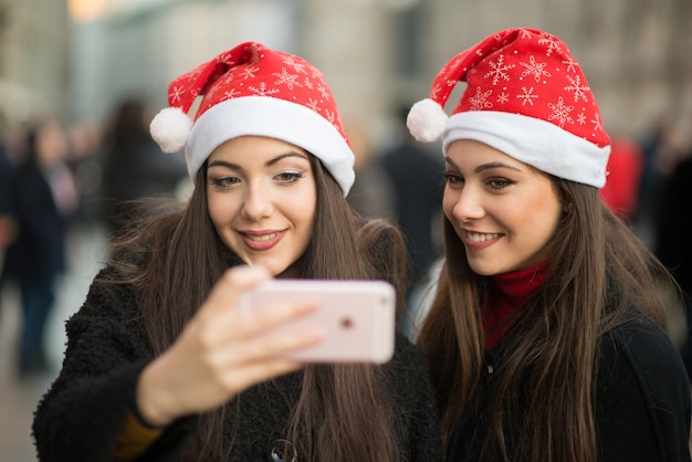 Giovani donne sorridenti in cappello di natale che cattura una maschera insieme