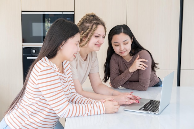 giovani donne spensierate diversità amici che usano il laptop divertendosi insieme nella cucina moderna a casa