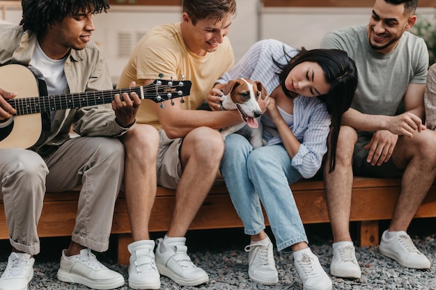 Giovani felici con chitarra e cane che trascorrono del tempo divertente vicino al camper cantando canzoni in campeggio insieme