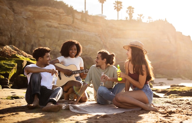 Giovani felici e diversi suonano la chitarra ascoltano musica bevono durante il picnic si divertono insieme