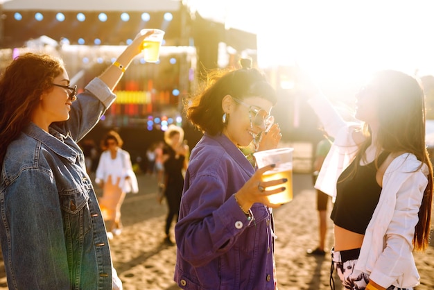 Giovani fidanzate che bevono birra divertendosi al festival musicale Celebrazione dell'amicizia Festa in spiaggia