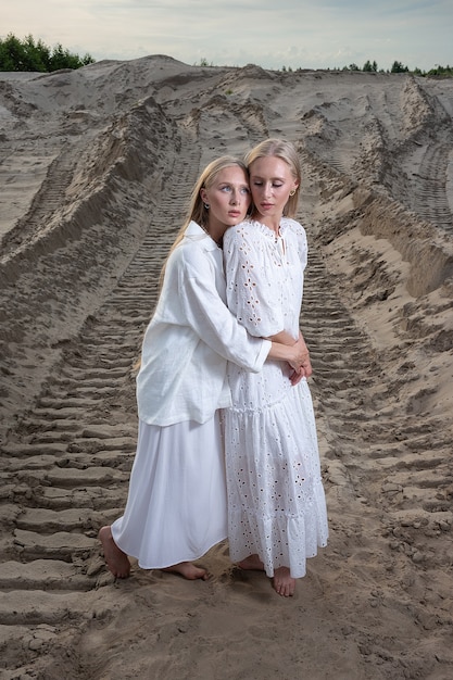 Giovani gemelli graziosi biondi che posano alla cava di sabbia in vestito bianco elegante