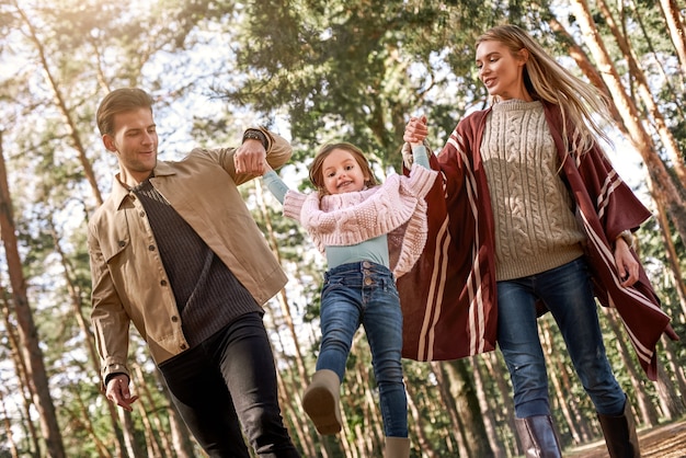 Giovani genitori con figlia piccola nella foresta autunnale. Mamma e papà che tengono la neonata. Vista dal basso