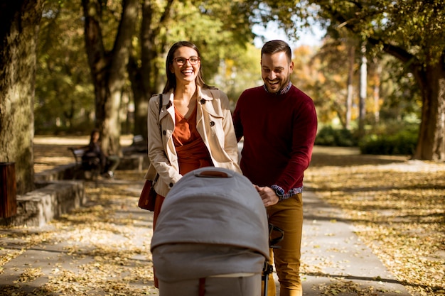 Giovani genitori felici che camminano nel parco e guidare un bambino in carrozzina