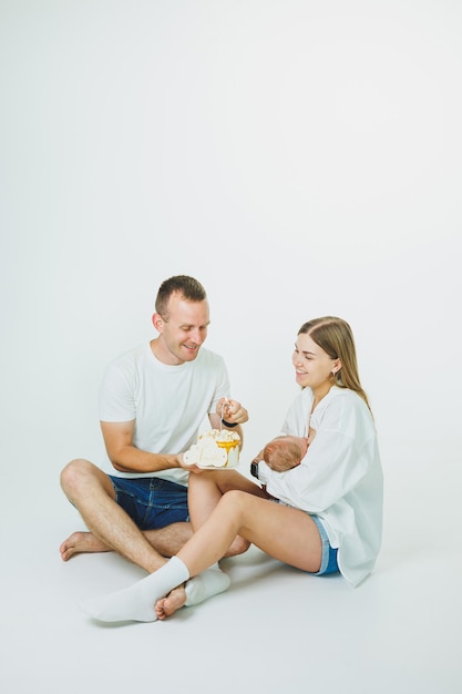 Giovani genitori felici con un bambino tra le braccia e una torta celebrano il primo mese di vita del bambino Mamma e papà con un neonato su uno sfondo bianco