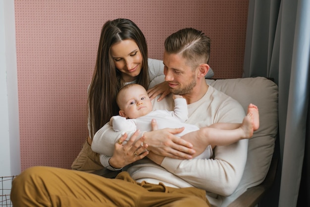 Giovani genitori felici tengono in braccio il loro bambino e sorridono guardandolo