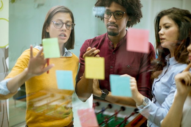 Giovani imprenditori discutendo davanti alla parete di vetro usando post-it note e adesivi