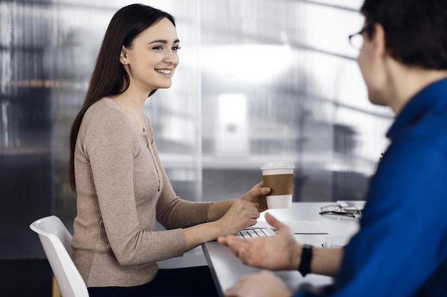 Giovani imprenditori parlano tra loro mentre fanno una pausa caffè in un ufficio moderno. Concentrarsi sulla donna. Concetto di successo aziendale.