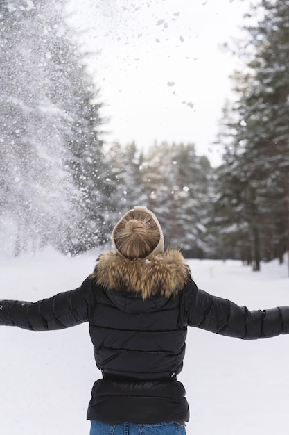 Giovani indossare piumino donna gettando neve in aria durante il freddo inverno day