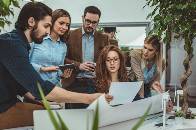 Giovani ingegneri intelligenti qualificati e qualificati stanno guardando al progetto di energia alternativa con miniature di turbine eoliche al tavolo.