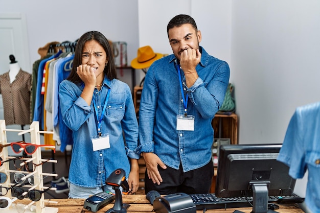 Giovani interrazziali che lavorano in boutique al dettaglio che sembrano stressati e nervosi con le mani sulla bocca che mordono il problema dell'ansia delle unghie