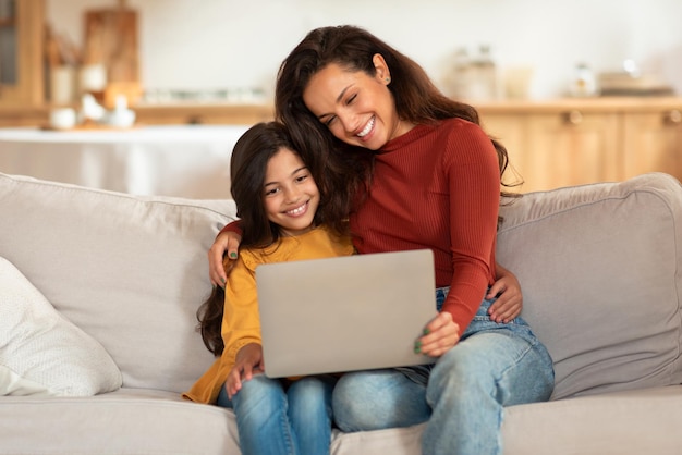 Giovani madri e figlie arabe felici che usano il portatile a casa