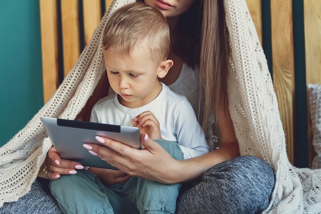 Giovani mamma e figlio con un tablet sotto un'accogliente coperta nel letto