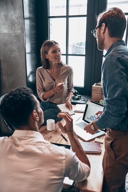 Giovani moderni in abbigliamento casual intelligente che discutono di affari mentre lavorano in ufficio