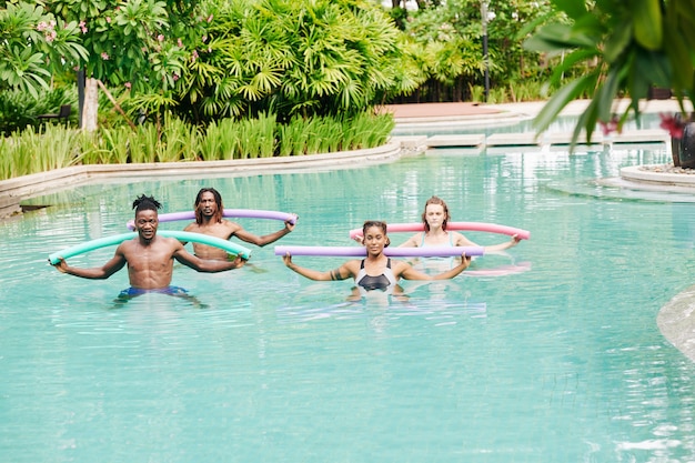 Giovani multietnici che fanno aerobica in acqua con spaghetti galleggianti nella piscina dell'hotel