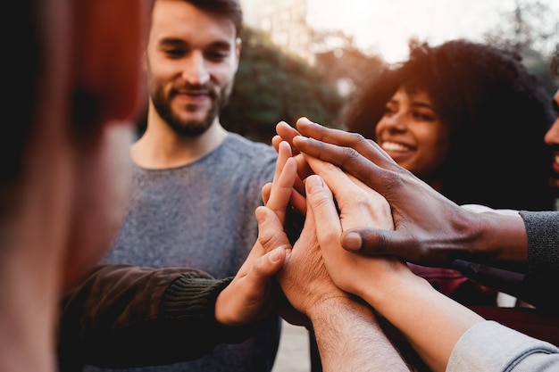 Giovani multirazziali che festeggiano insieme mentre impilano le mani all'aperto - Focus on hands