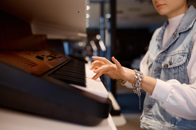 Giovani pantaloni a vita bassa femminili che giocano la tastiera di pianoforte eclettica al negozio musicale