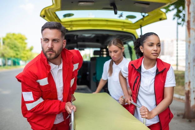 giovani paramedici che spostano in fretta la barella dell'ambulanza dalla macchina paramedici in uniforme che portano la barella fuori dall'ambulanza