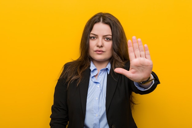 Giovani plus size donna d'affari caucasica in piedi con la mano tesa che mostra il segnale di stop, impedendoti.