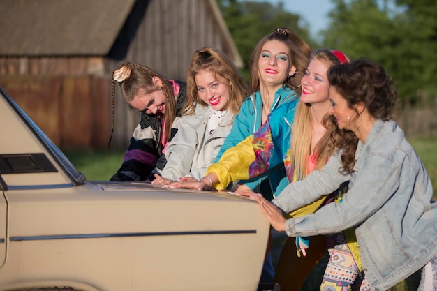 Giovani ragazze allegre spingono una vecchia macchina Donne nello stile degli anni '90