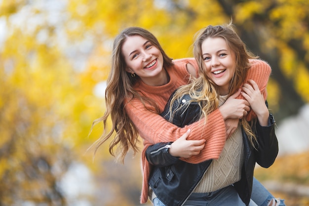 Giovani ragazze graziose divertendosi all'aperto in autunno. Amici allegri in autunno