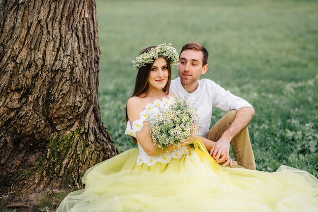 Giovani sposi felici che si siedono sull'erba vicino all'albero nel parco