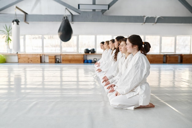 Giovani studenti di aikido che indossano kimono seduti sul pavimento in fila